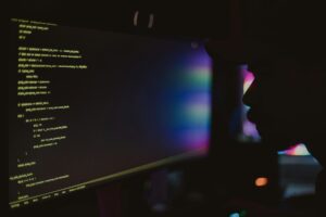 This is an image of a man sitting in the dark looking at some code on a computer.