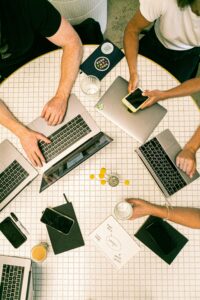 This is an overhead picture of people sitting at a table with their phones and laptops.