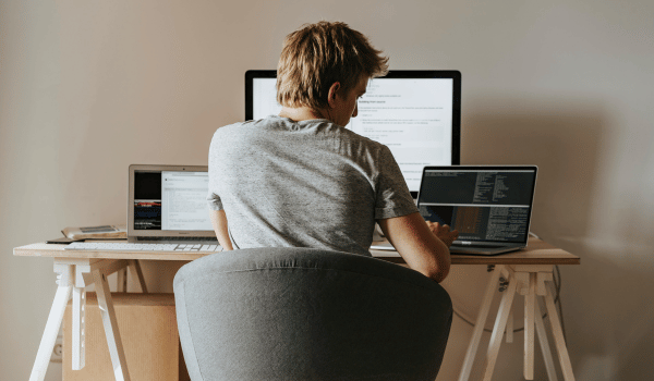 This is an image of a man sitting at a desk with two open laptops and a monitor in front of him.