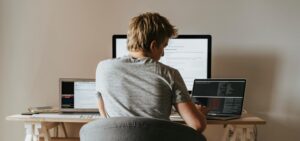 This is an image of a man sitting at a desk with two open laptops and a monitor in front of him.